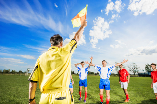 Linesman showing offside with his flag. Disappointed soccer players are in the background.   
