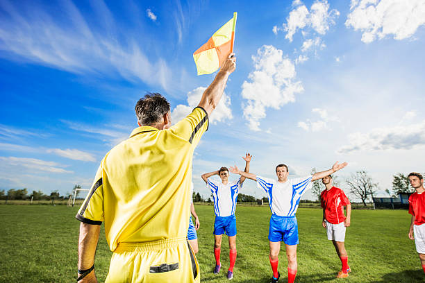 Soccer match. Linesman showing offside with his flag. Disappointed soccer players are in the background.    offside stock pictures, royalty-free photos & images