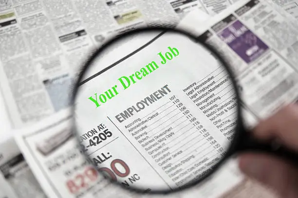 Magnifying glass over a newspaper classified section, with Your Dream Job text