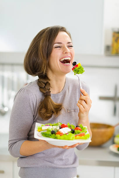 glückliche junge frau essen frischer salat - stereotypical housewife women domestic kitchen brown hair stock-fotos und bilder