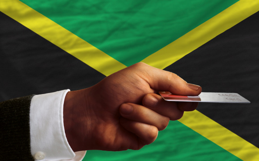 man stretching out credit card to buy goods in front of complete wavy national flag of jamaica