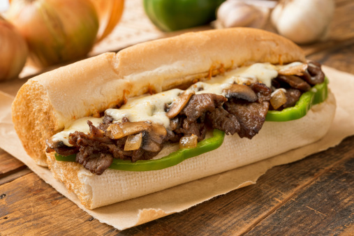 A delicious oven baked steak and cheese submarine sandwich with mushrooms, green peppers, and onion.