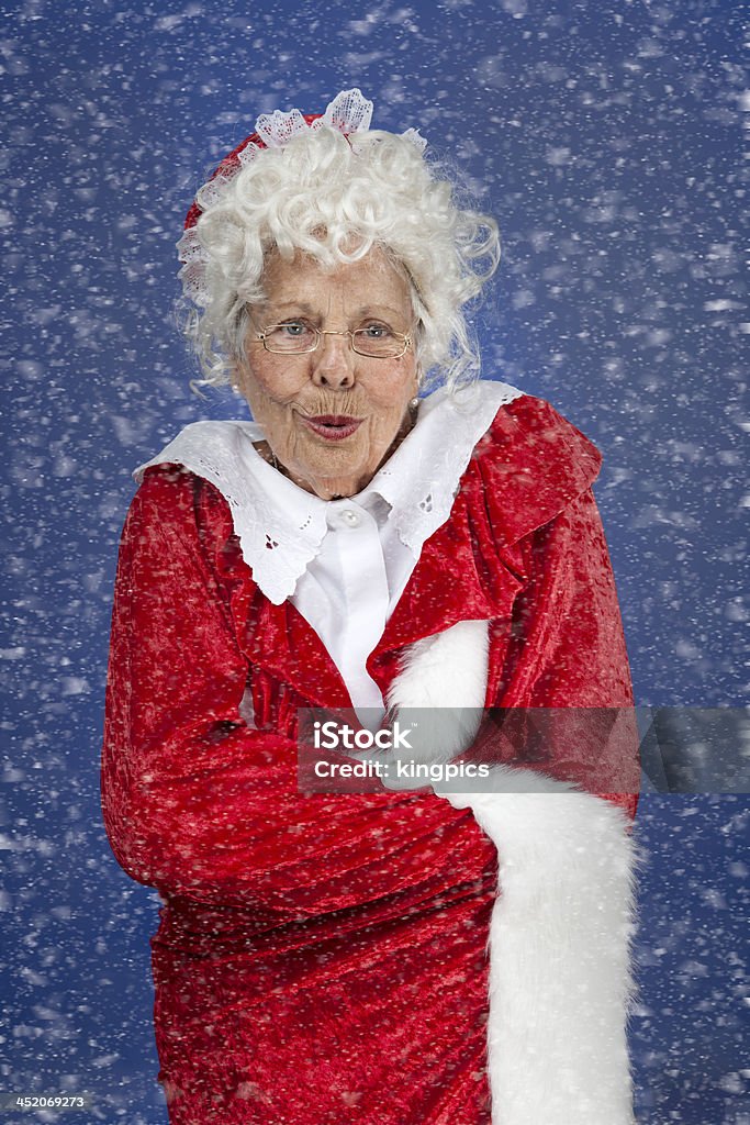 Mrs Claus outside in the snow A vertical image of Mrs Claus shivering outside in the snow. Blue Background Stock Photo