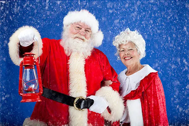 A horizontal image of Santa holding a lantern to light the way for Mrs Claus.