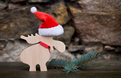 a wooden moose with santa hat standing in a simple backdrop,