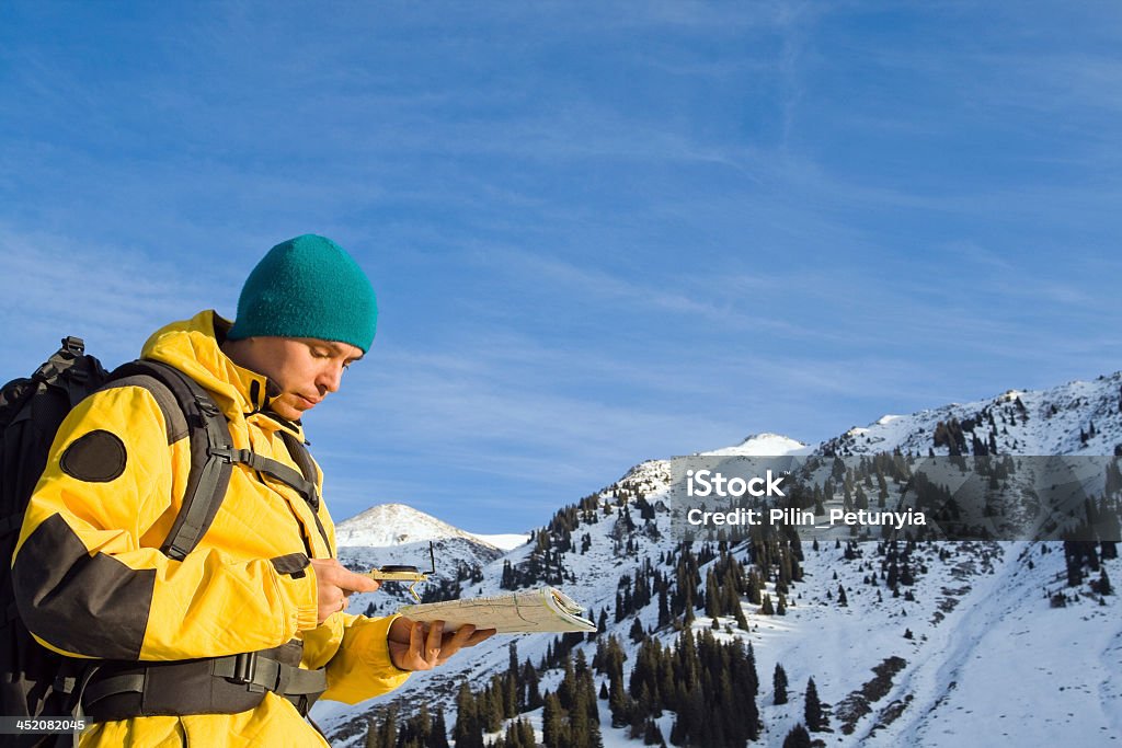 Mountain climber near snow capped peak using map compass Climbing young adult with map and compass. Aerial view of mountain and blue sky Navigational Compass Stock Photo