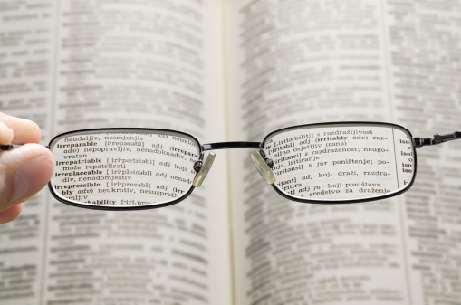 out of focus dictionary with hand holding a glasses that correct the vision