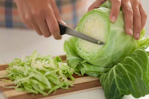 Woman cuts cabbage on cutting board in kitchen.