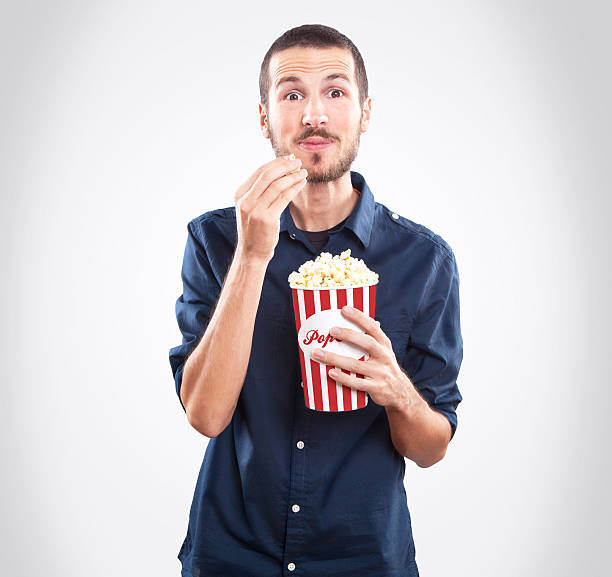 Jovem homem assistindo a um filme e comer pipoca - foto de acervo