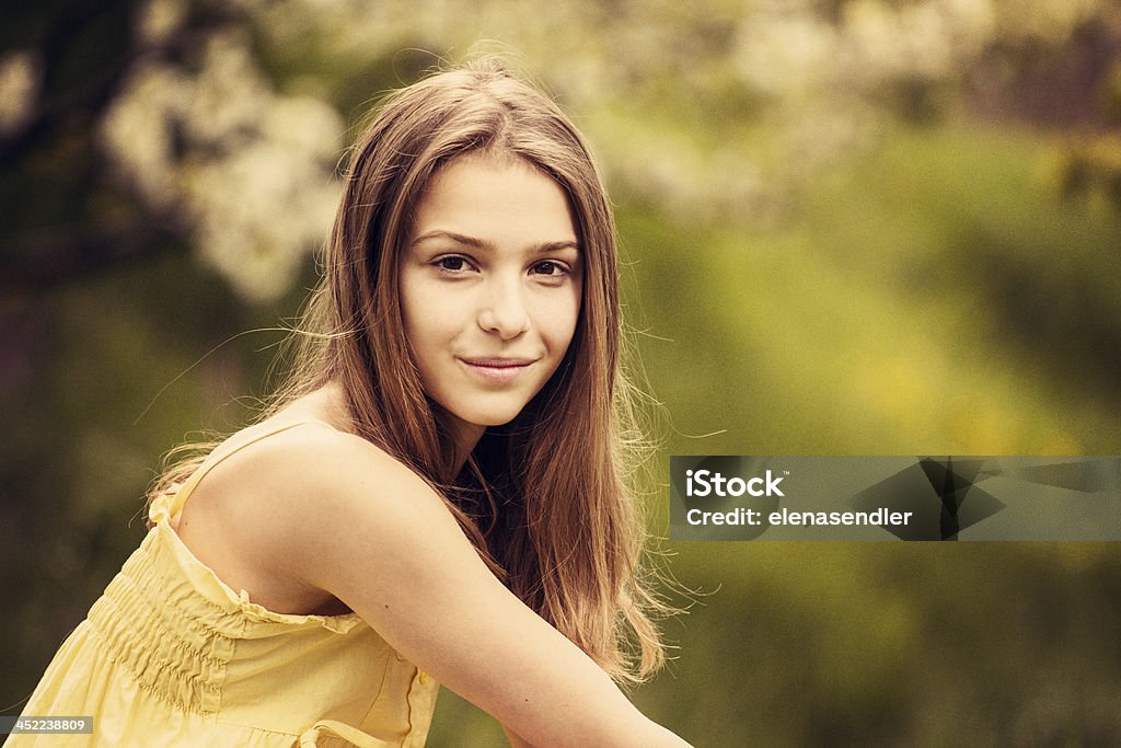Young girl smilling Young girl in a sleevless yellow dress, sitting on a bench, blurred green background 12-13 Years Stock Photo