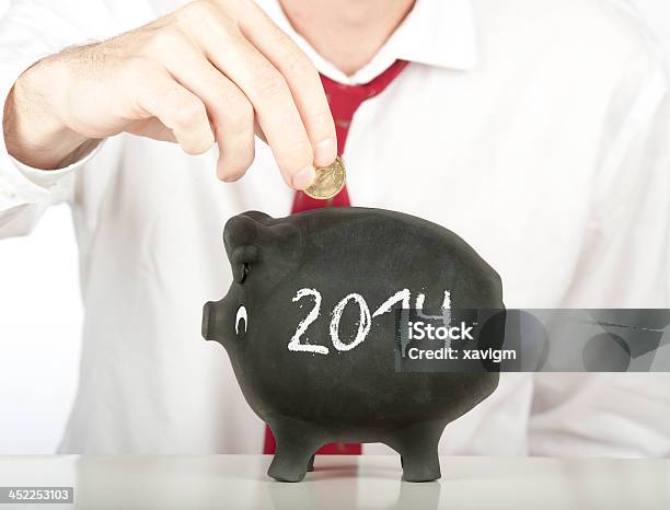 Businessman Putting Money On A 2014 Piggy Bank Stock Photo - Download Image Now - 2014, Adult, Adults Only