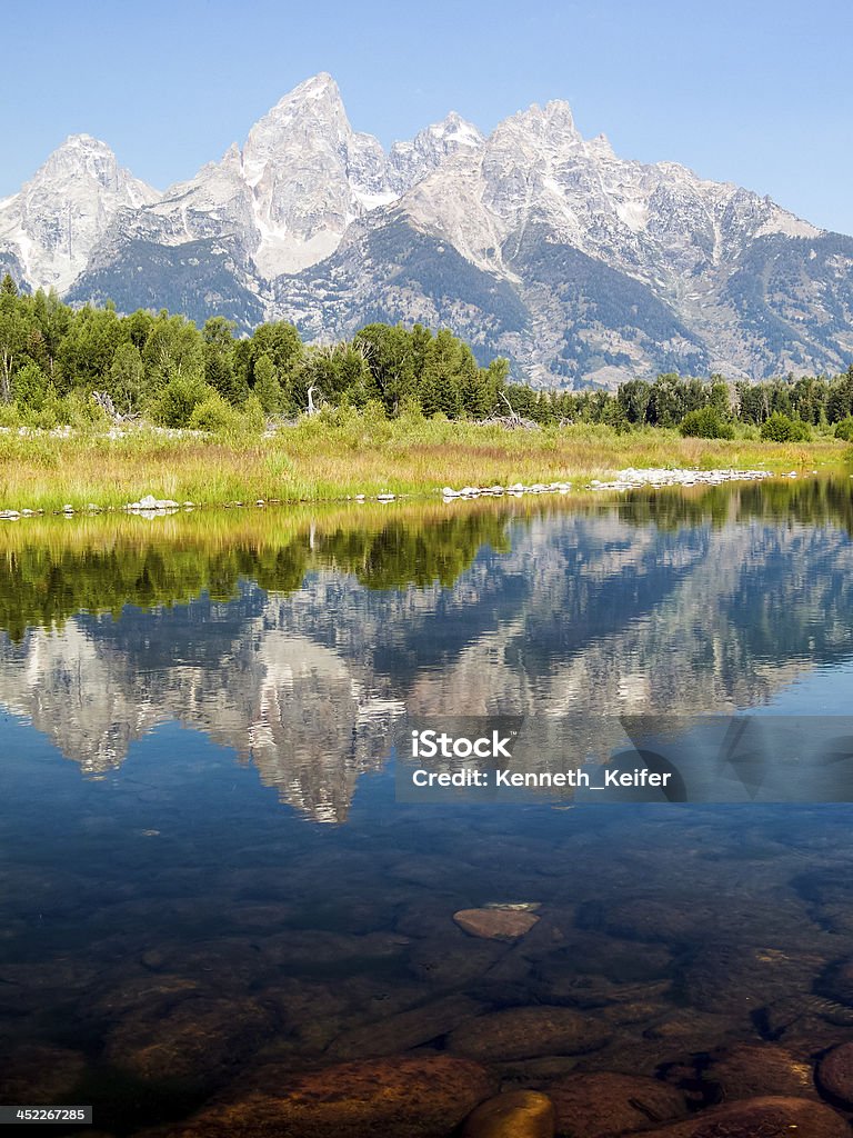 Majestic Reflection The Cathedral Group of the Teton Mountain Range is reflected on the waters of the Snake River with rocks visible beneath the surface at Schwabacher;s Landing in Grand Teton National Park, near Jackson Hole, Wyoming, USA. Awe Stock Photo