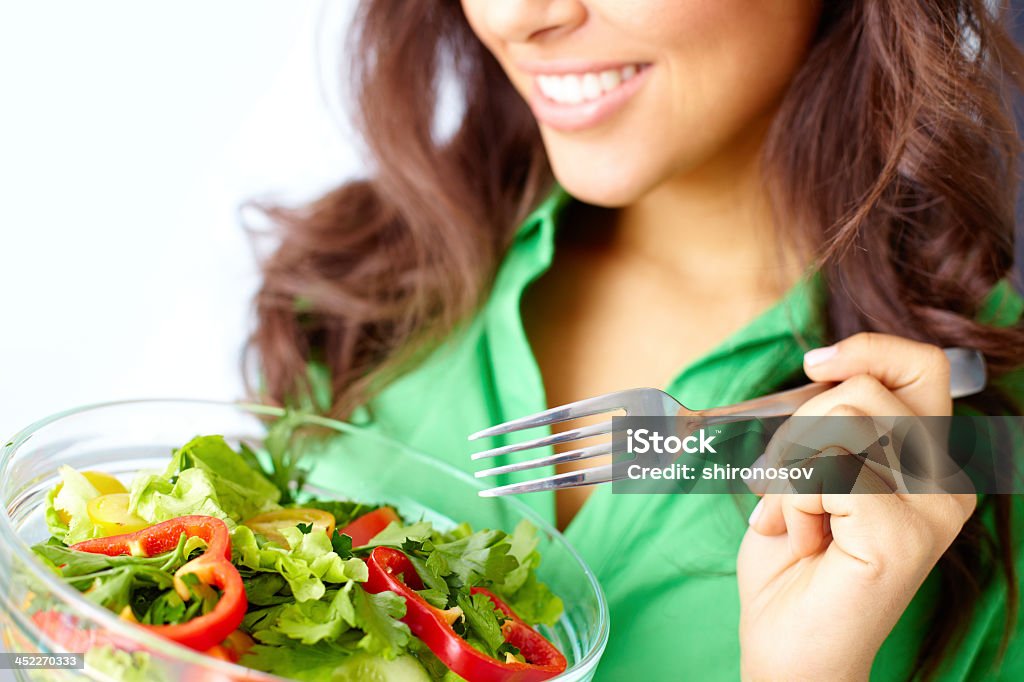 Focus on clear bowl of salad held by smiling woman on a diet Close-up of pretty girl eating fresh vegetable salad Adult Stock Photo