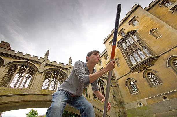 Punting on the Cam Lazy Sunday afternoon on the River Cam in Cambridge, England, Good looking young man punting underneath a University stone bridge. couple punting stock pictures, royalty-free photos & images