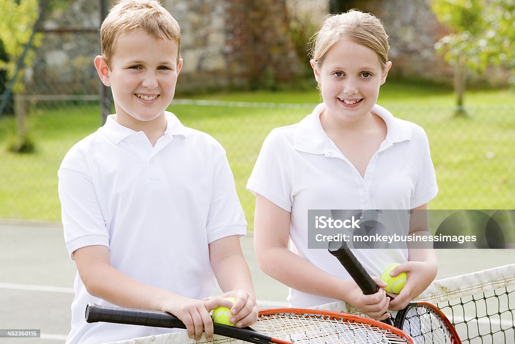 Deux jeunes amis avec raquettes sur souriant de tennis court - Photo de Activité libre de droits