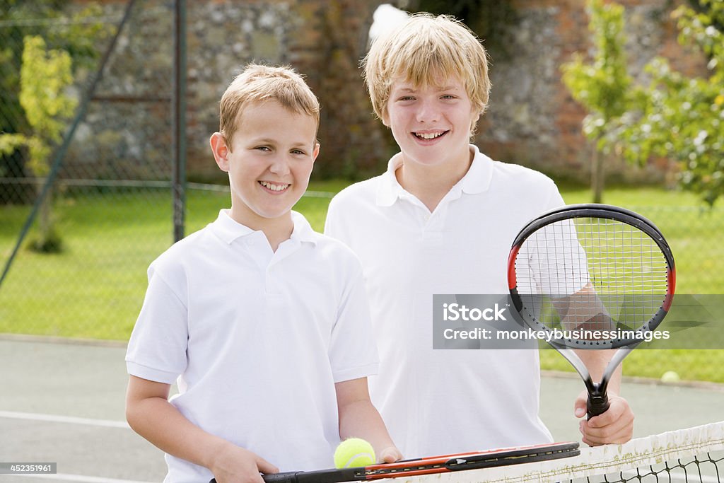 Deux jeunes amis masculins avec raquettes sur souriant de tennis court - Photo de Blanc libre de droits