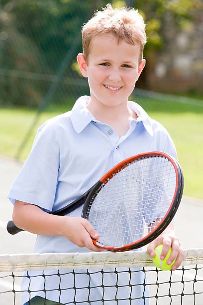 istock Young boy with racket on tennis court smiling 452353909