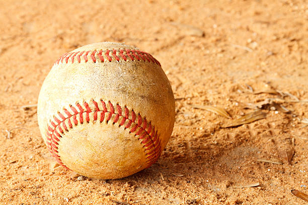 An old dirty grunge baseball on the dirt infield of a baseball field.
