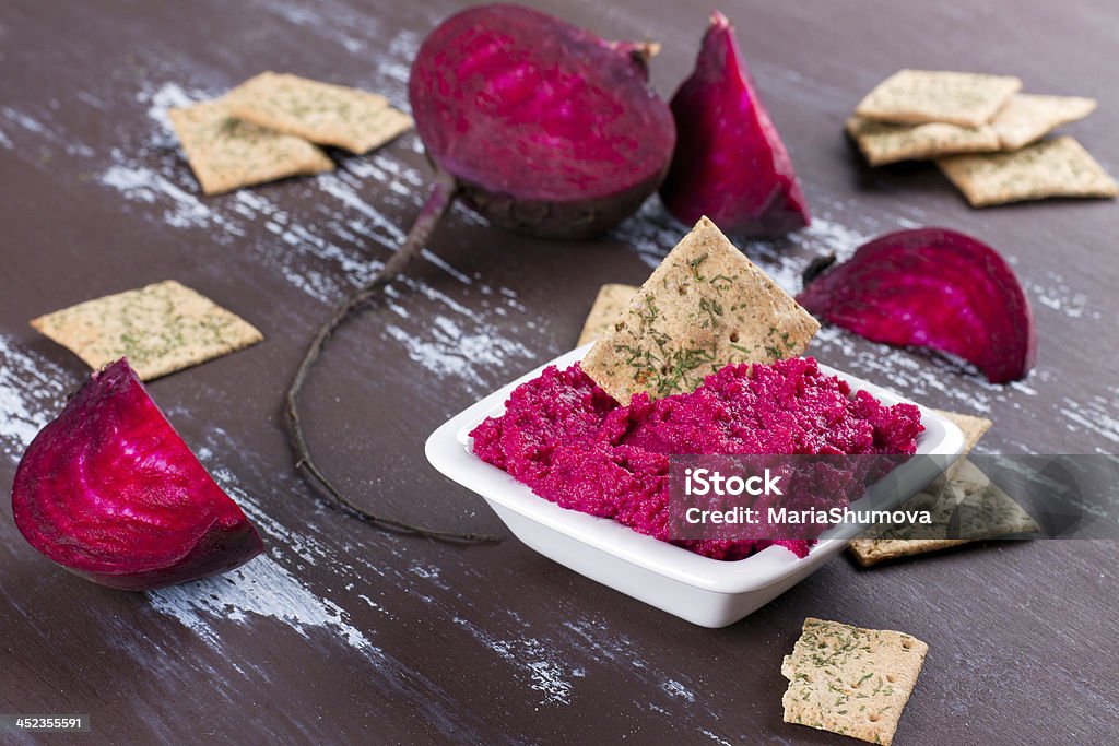 Dish of beetroot hummus with crackers on a wooden table Portion of beetroot hummus with raw beetroot and crackers on background Cracker - Snack Stock Photo