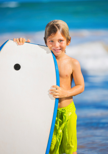 Happy Young boy having fun at the beach on vacation, with boogie board
