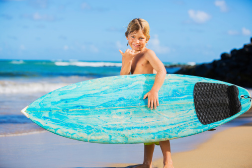 Young surfer, happy young boy at the beach with surfboard