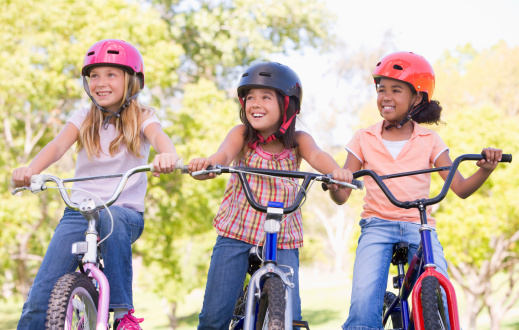 Three young girl friends outdoors on bicycles looking away from camera smiling wearing helmets