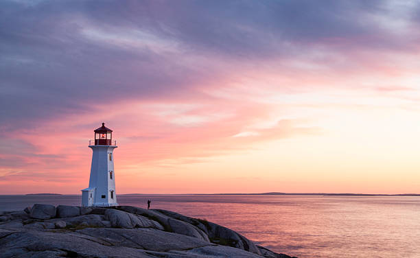Lighthouse at Peggy's Cove Nova Scotia Lighthouse at Peggy's Cove, Nova Scotia, Canada.  Person in silhouette taking a photograph visible beside lighthouse. beacon photos stock pictures, royalty-free photos & images