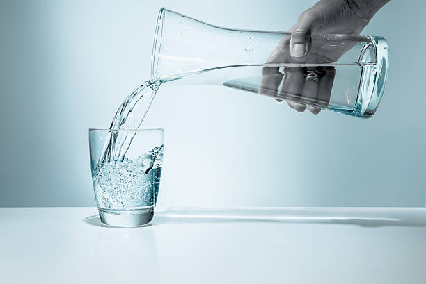 Pouring water into a glass Pouring water from pitcher into a glass blue jug stock pictures, royalty-free photos & images
