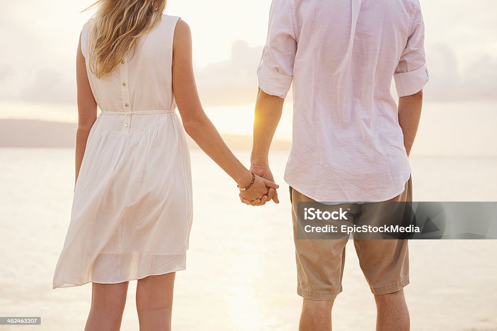 Couple holding hands at sunset on beach Couple holding hands at sunset on beach. Romantic young couple in love Adult Stock Photo