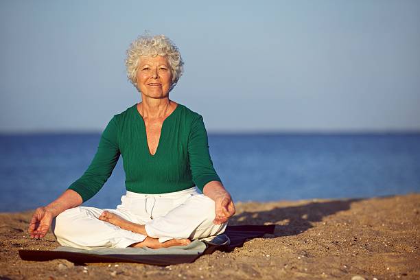 istock Senior woman meditating on sandy beach 452468997