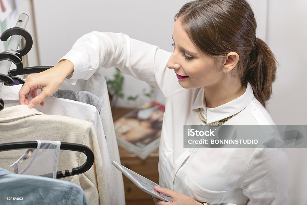 Fashion woman choosing a piece for the new collection. Fashion woman with digital tablet working in her office. Adult Stock Photo