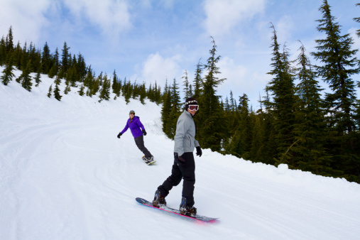 A couple snowboards down some groomed ski runs at a mountain resort.