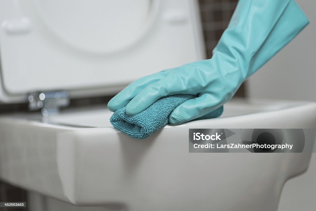 Person cleaning the toilet seat in rubber gloves Hand of a person cleaning the toilet seat in rubber gloves with a sponge disinfecting the underside for germs and bacteria while performing household chores Bacterium Stock Photo