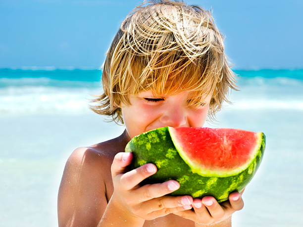 istock boy eating a slice of watermelon on the beach 452526779