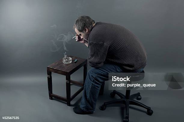 Depressed Young Man Sitting On A Chair Smoking Cigarette Stock Photo - Download Image Now