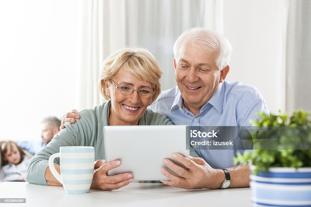Senior couple with digital tablet Cheerful senior couple sitting by the table at home and using a digital tablet together. 60-69 Years Stock Photo
