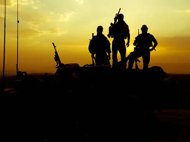 Silhouette of 3 soldiers at sunset with weapons