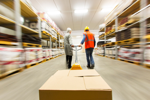 Two warehouse workers pulling pallet truck with boxes.....blurred motion