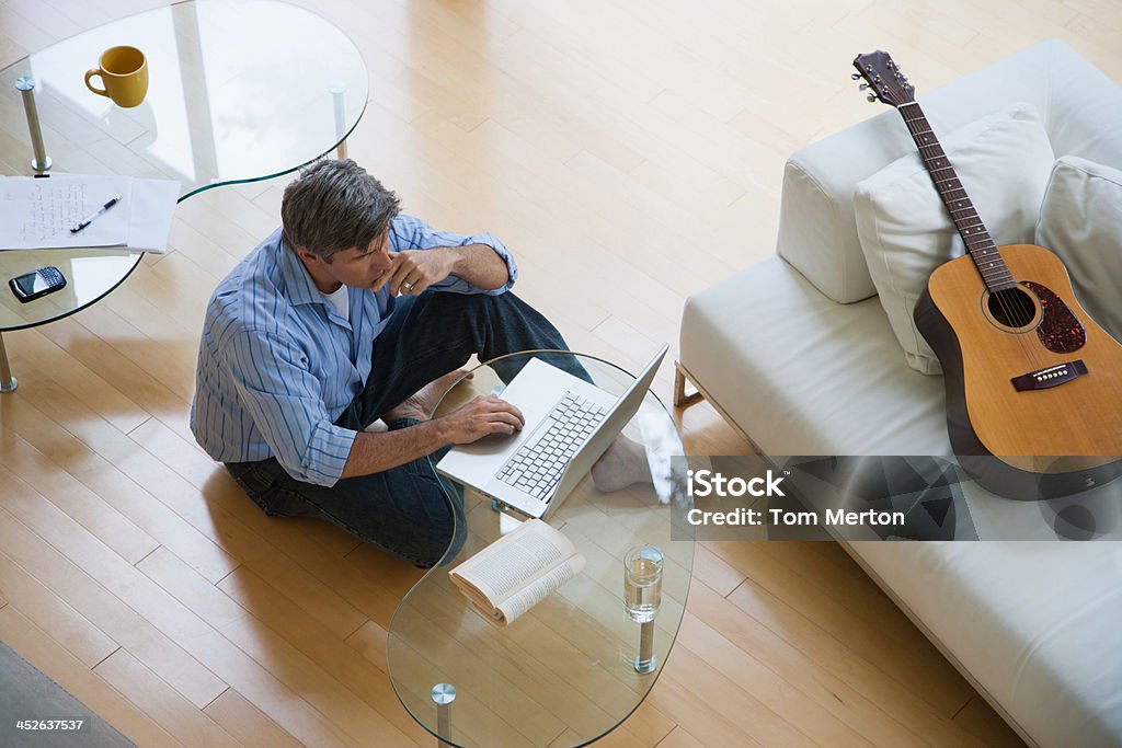 Man in living room sitting on floor using laptop  Coffee Table Stock Photo
