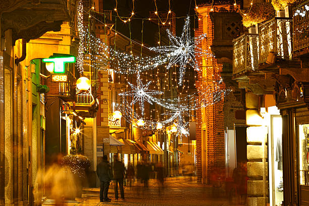 People walking in evening street illuminated and decorated for Christmas and New Year celebrations in Alba, Italy.