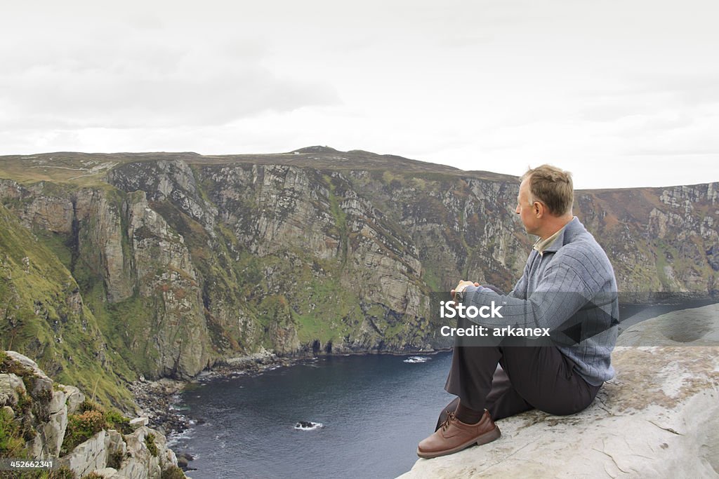 Contemplation. Man sitting on rock and looks away towards horizon. Active Lifestyle Stock Photo