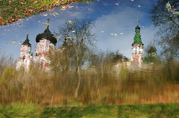 Water surface of the autumn lake is reflecting the blue sky, Orthodox churches and bare trees.