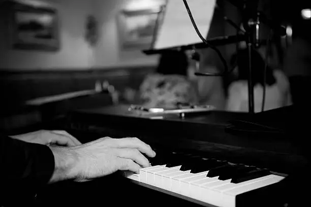 Close up black and white image of a man playing piano in a bar.