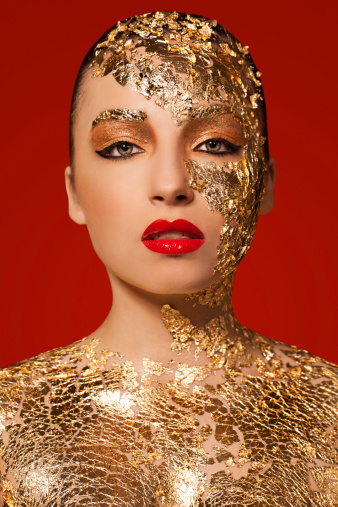 Beautiful woman with gold leaf on her face and body, red lips and black eyeliner.