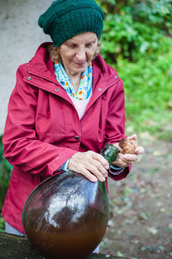 Senior woman in country with two wine demijohn take from home cellar,