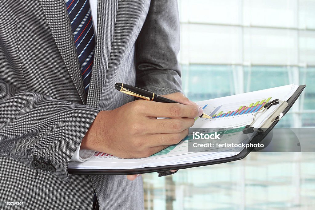 A man writing with a ballpoint pen on a chart on a clipboard businessman writing on paper in the office Adult Stock Photo