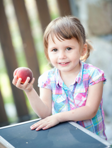 Baby girl with a peach in her hand. Selective focus.