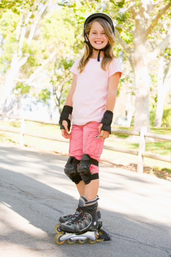 Young girl outdoors on inline skates smiling at camera wearing protective gear