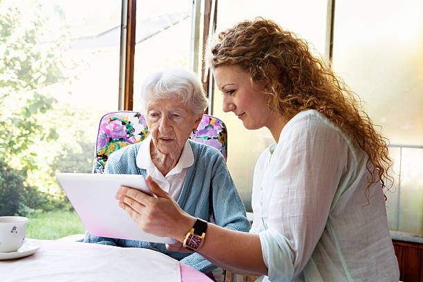 senior woman and digital tablet young caregiver showing something to senior woman, 90 years old, on digital tablet community outreach stock pictures, royalty-free photos & images