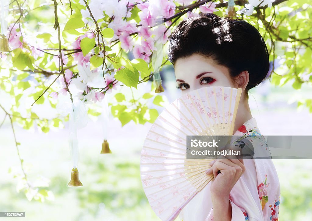 Geisha with fan in the garden Asian style portrait of young woman with fan in the blooming garden Adult Stock Photo